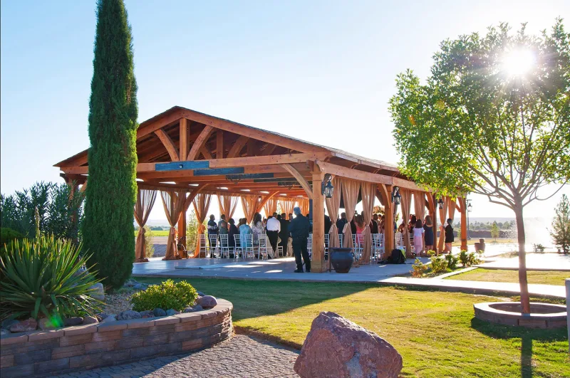 A redwood pavilion with draped curtains set for a wedding at sunset